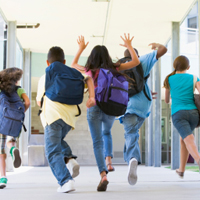 Mehrere Schüler sind von hinten fotografiert, wie sie freudig den Schulflur entlanglaufen und -springen.